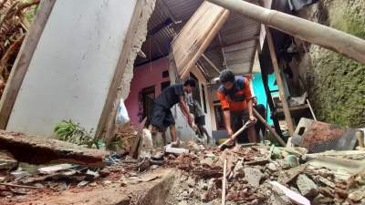 Maulana dibantu tetangganya saat membersihkan puing-puing rumahnya akibat diterjang longsoran tanah dan akar pohon bambu.