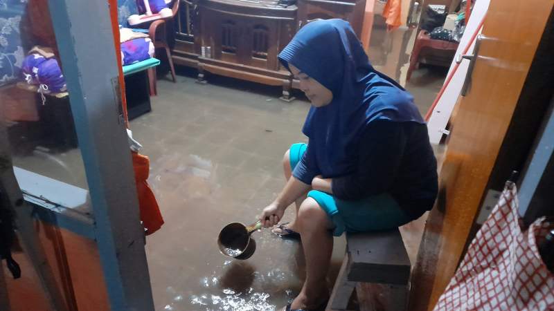 Salahsatu warga di RW 01 Pondok Betung sedang mengeringkan air yang masuk rumah menggunakan gayung.