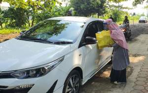 Salah satu guru saat memberikan rapor secara drive thru kepada orang tua siswa, Kamis (18/6).